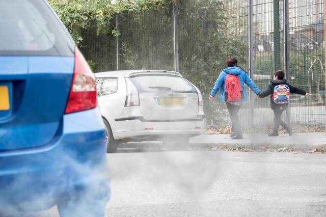 Parent and child walking to school past cars with billowing exhausts