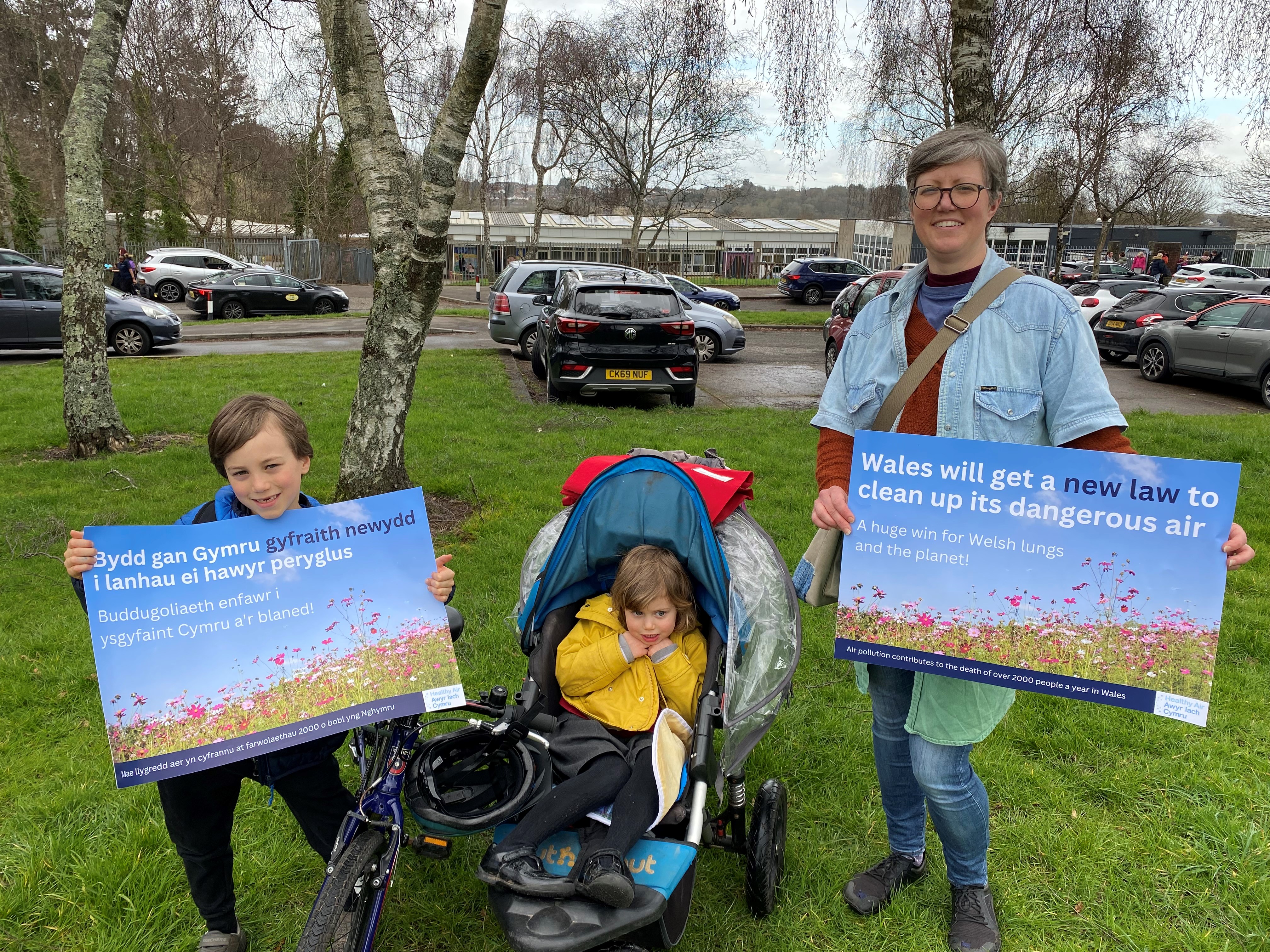 Photo of lady with two children, holding up a poster