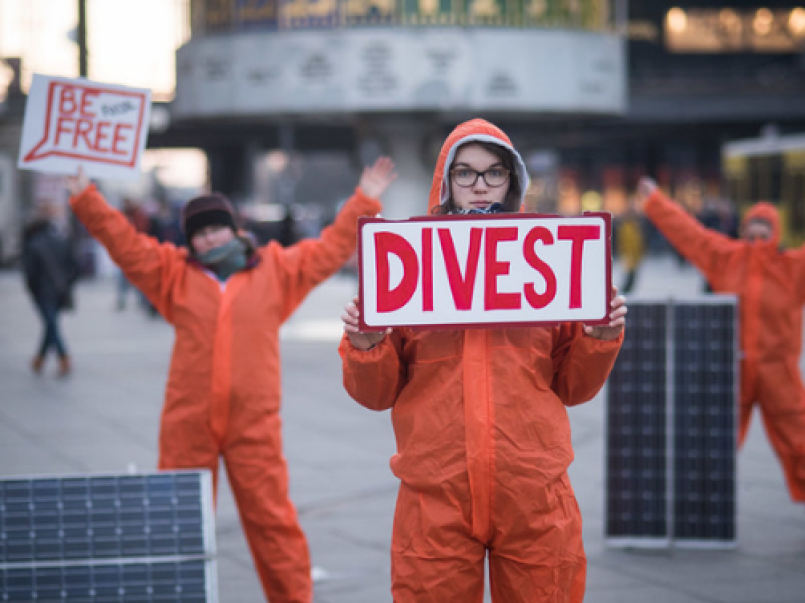 Llun o bobl yn dal placard 'divest'