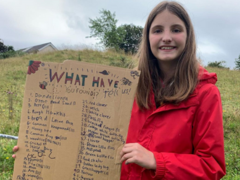 Child holing up a board listing the plants and bugs she has found