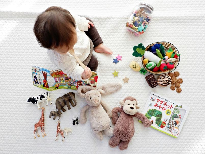 Image taken from above of young girl on rug surrounded by toys