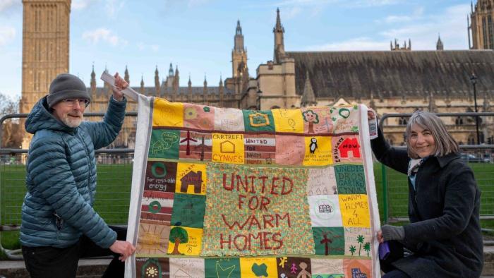 Two people holding up a quilt outside Westminster
