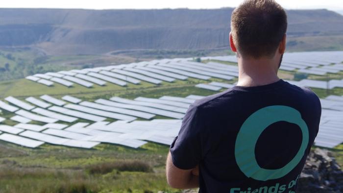 Person with FOE teeshirt looking at solar panels on a hillside